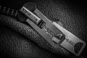 Close-up of a metallic zipper pull on a textured fabric background.