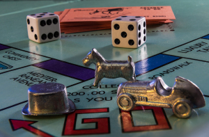 A silver car, a dog, and a top hat on a Monopoly board with dice in the background.