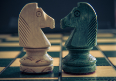 Two chess knights, one white and one green, poised on a checkered board, embodying silent rivalry.