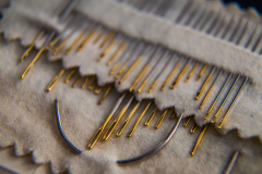 A close-up of sewing needles arranged on a soft fabric surface.