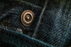 Close-up of a shiny metal button on dark denim fabric, showcasing texture and detail.