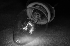A close-up of a vintage light bulb with visible filament glowing in black and white.