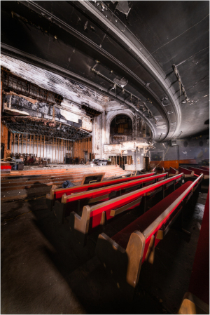 Abandoned theater with empty red seats and peeling walls, shadows lurking in corners.