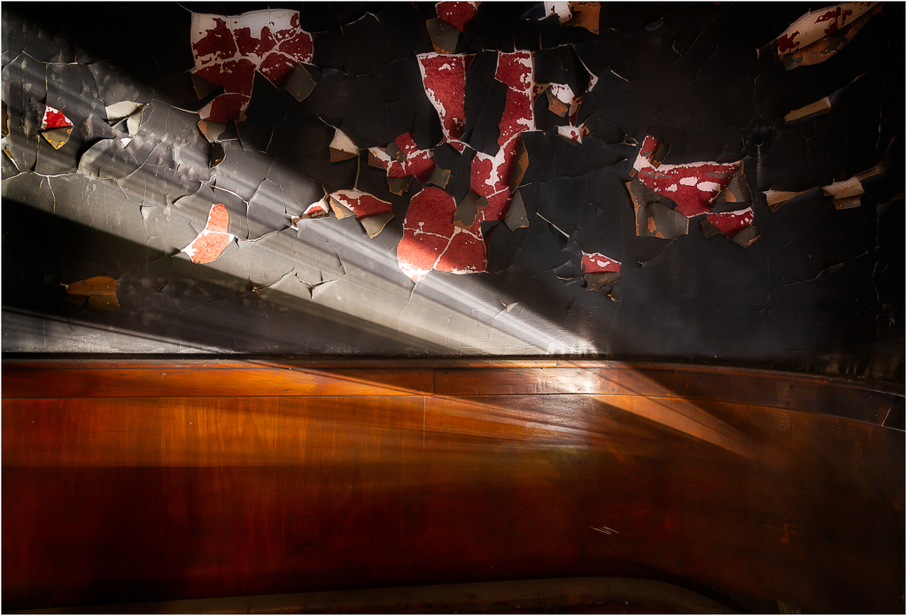 Abandoned theater interior with peeling paint and shadowy beams of light.