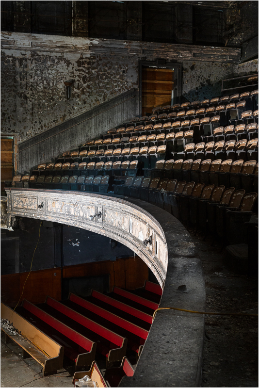 Abandoned theater with peeling walls and empty seats, shadows lurking in the corners.