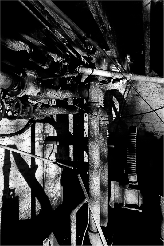 A dimly lit industrial space with rusted pipes and shadows creeping along the walls.