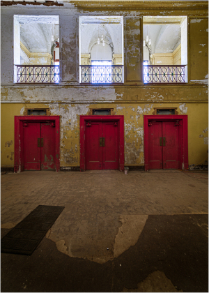 Three red doors in a dilapidated theater with peeling walls and a hint of grandeur.