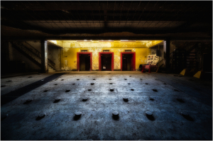Interior of an abandoned theatre with three red doors and a shadowy floor.