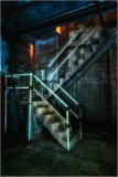 A dimly lit, worn staircase in an industrial setting with peeling paint and shadows.