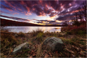 A vibrant sunset over a lake, with colorful clouds and rocky shore.