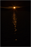 A glowing sun rises above dark waters, casting shimmering reflections.