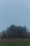A fog-shrouded mound amidst desolate fields, crowned with spectral trees.