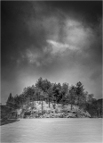 A rocky island with trees under a cloudy sky, captured in black and white.
