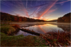A tranquil lake reflects a surreal sunset with vibrant clouds and misty surroundings.