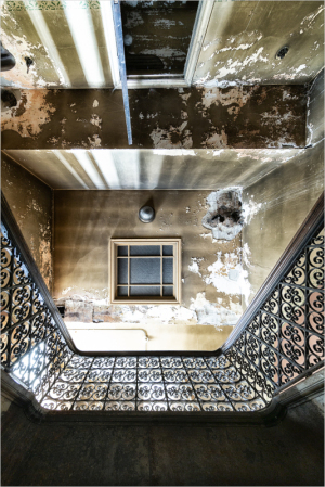 A downward gaze reveals a staircase adorned with intricate ironwork and peeling walls.