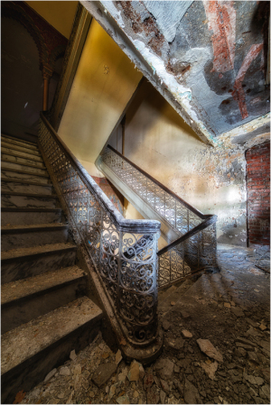 Intricate staircase with ornate railing in a historic building, showing wear and decay.