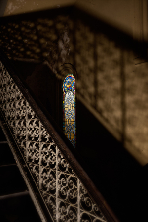 Stained glass window casts colorful light on ornate staircase railing.