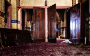 Open wooden doors reveal a dusty, abandoned interior with faded colors and scattered debris.