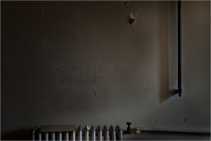 A dimly lit wall with a pipe and a row of white objects on the floor.