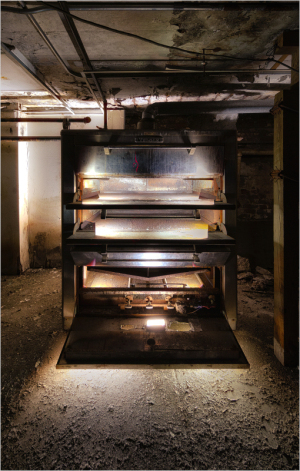 An old, rusty oven with three stacked compartments, illuminated from below.
