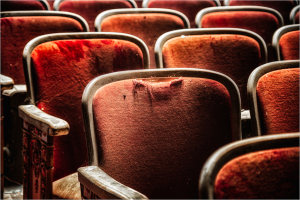 Worn red theater seats with ornate armrests, hinting at past grandeur.