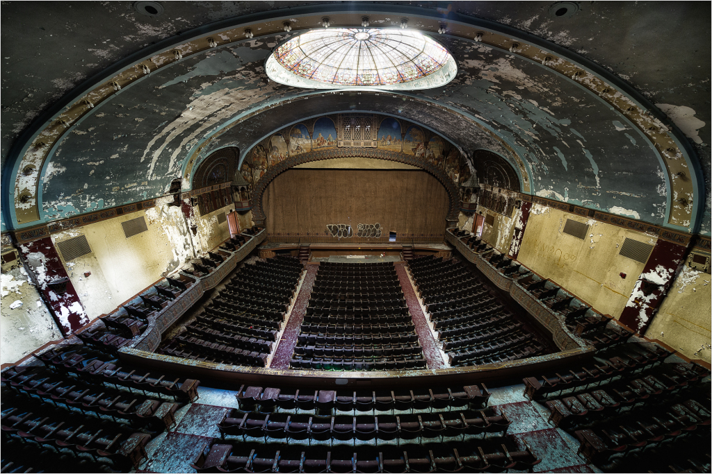 An abandoned theater with ornate ceiling and empty seats, evoking lost grandeur.