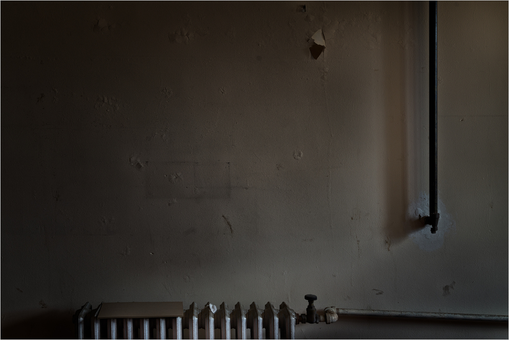 A dimly lit wall with a pipe and a row of white objects on the floor.