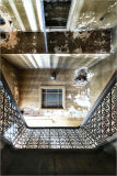 A downward gaze reveals a staircase adorned with intricate ironwork and peeling walls.