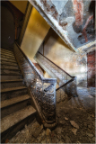 Intricate staircase with ornate railing in a historic building, showing wear and decay.