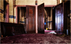 Open wooden doors reveal a dusty, abandoned interior with faded colors and scattered debris.