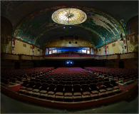 An empty theater with rows of red seats and a colorful ceiling dome.