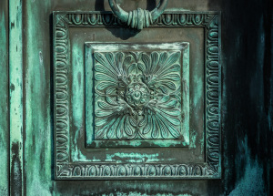 Weathered metal door knocker with intricate design and green patina
