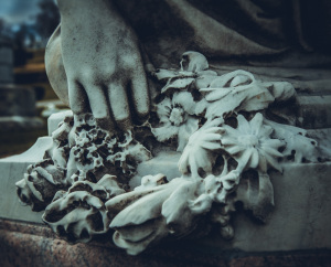 A close-up of a stone hand grasping wilted flowers, ghostly and dramatic.