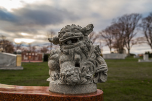A fierce stone guardian lion statue stands watch over a peaceful landscape, shrouded in drama.