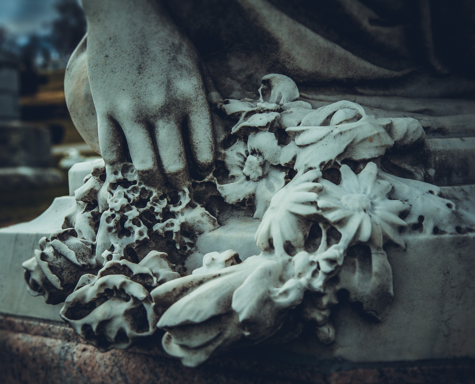 A close-up of a stone hand grasping wilted flowers, ghostly and dramatic.