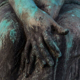 Close-up of weathered hands resting on a thigh, textured and raw.