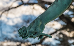 A bronze hand clutching a rose, poised in a dramatic gesture.