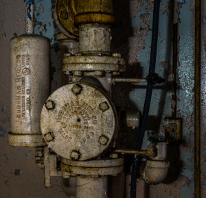 Close-up of an old, rusty water valve and pipe system with peeling paint.