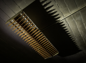 Rusty metal grate hanging from a ceiling, casting sharp shadows on the wall.