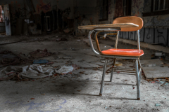 An abandoned classroom desk with an orange seat in a dilapidated room.