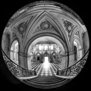 A grand staircase leads to a bright doorway in a beautifully detailed hall.