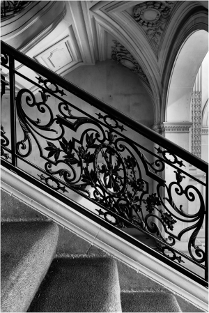 Black and white image of an ornate staircase railing with intricate designs.