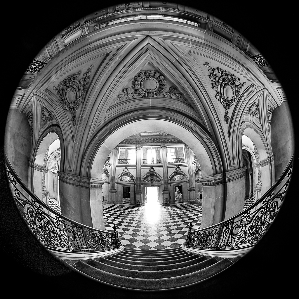 A grand staircase leads to a bright doorway in a beautifully detailed hall.