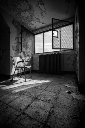 Abandoned room with a chair, open window, and peeling walls, showcasing natural light.