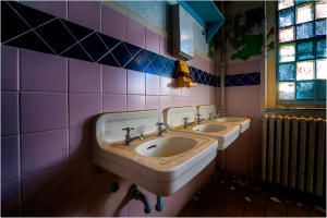 Three vintage sinks with faucets in a tiled restroom setting.