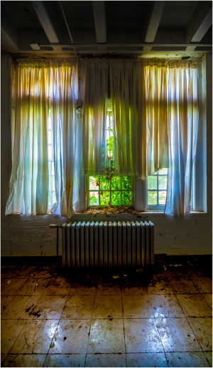 Interior space with large windows and curtains, revealing a radiator and tiled floor.