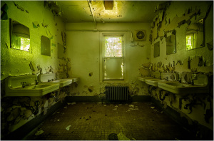 Interior of a dilapidated restroom with peeling walls and multiple sinks.
