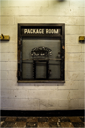 Metal mesh window labeled 'PACKAGE ROOM' in a brick wall setting