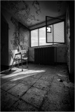 Abandoned room with a chair, open window, and peeling walls, showcasing natural light.