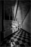A white sink mounted on a wall in a dimly lit attic space with wooden beams.